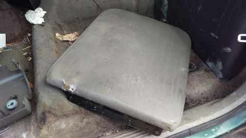 1994 Ford Bronco - The interior of a vehicle shows a worn, gray center console lid with visible damage. The surrounding carpet is dirty and littered with debr…