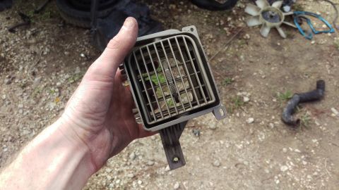 1994 Ford Bronco - A hand holds a gray car vent with metal slats, showing some green debris inside. In the background, a black fan and a black hose lie on the…