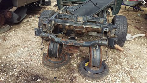 1994 Ford Bronco - The rear axle and frame of a disassembled vehicle, likely a truck or SUV, is shown resting on tires in a junkyard setting. The frame is hea…