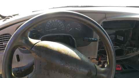 1994 Ford Bronco - The interior of a vehicle shows a steering wheel with a Ford logo and a dashboard with gauges. The center console appears to be disassemble…