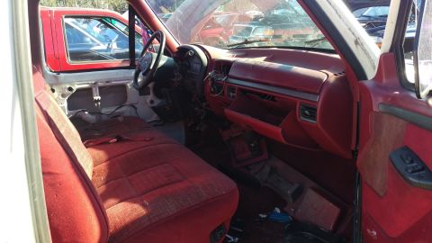 1994 Ford Bronco - The interior of a red and white 1990s pickup truck is shown, featuring a red bench seat, red dashboard, and a steering wheel. The door pane…