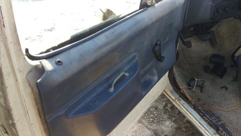 1994 Ford Bronco - The interior of a vehicle shows a dark blue door panel with a metal pull handle and a window crank. The floor is covered in tan carpet and…