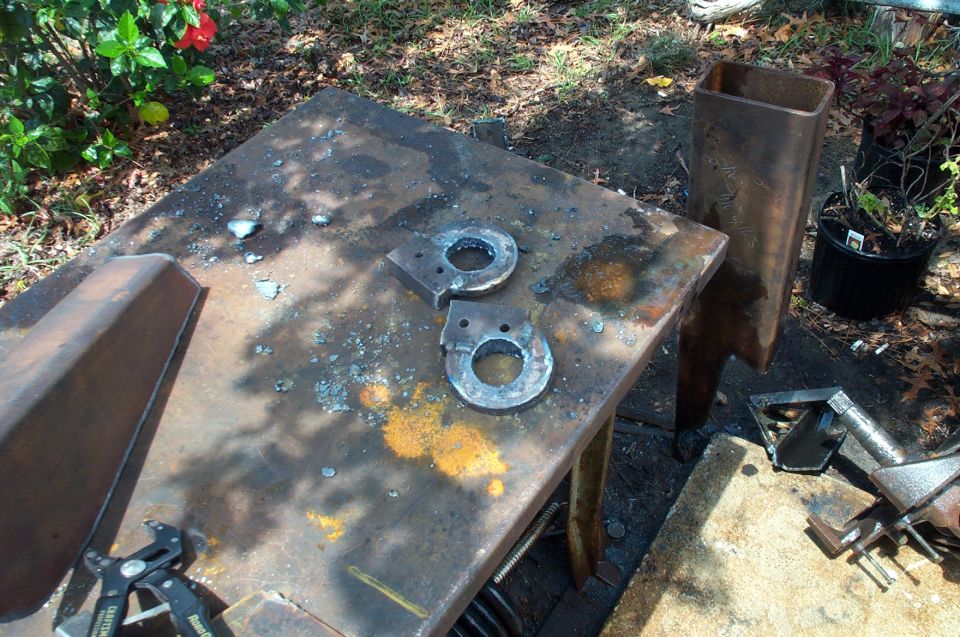 Two metal circular pieces with holes on a rusty metal table outdoors.
