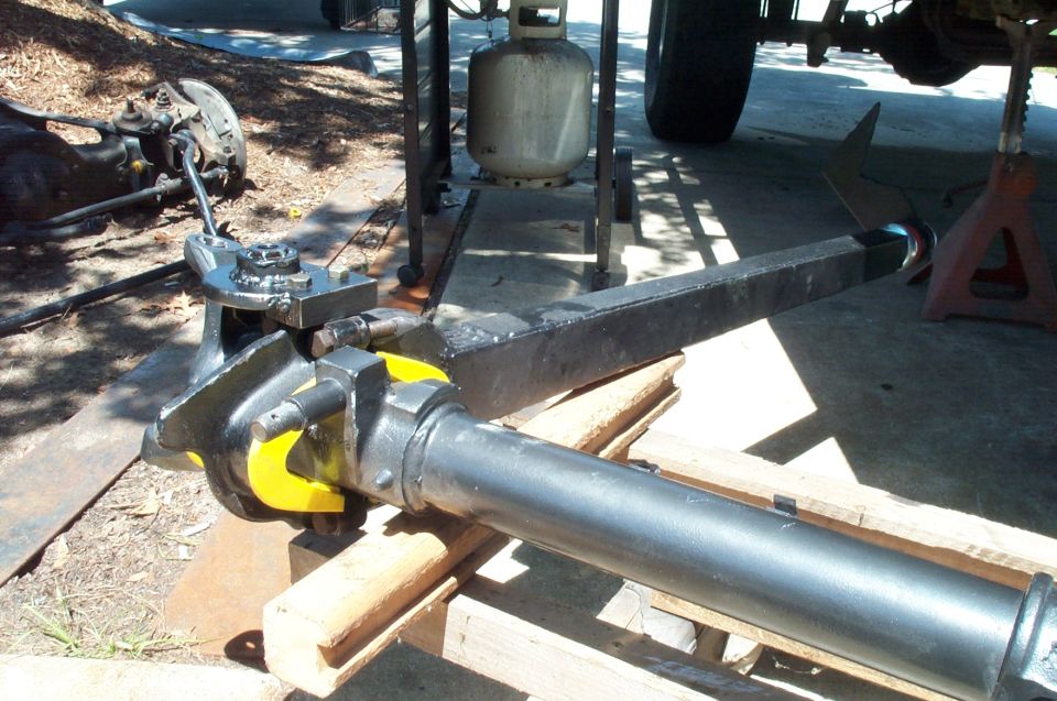 Close-up of a vehicle axle assembly with yellow accents, supported by wood and a jack stand.
