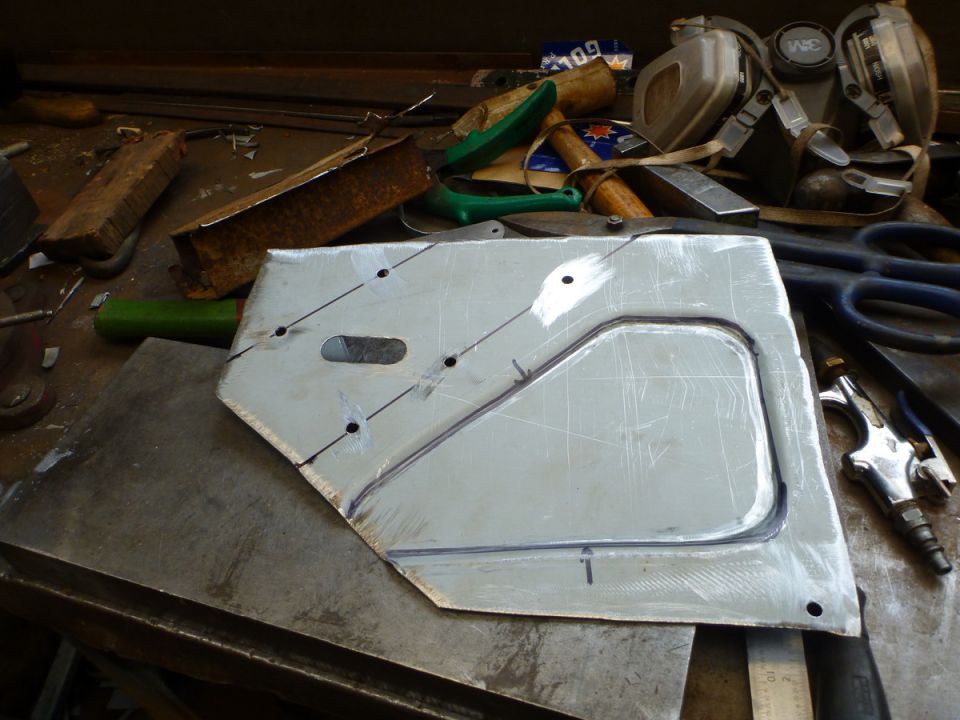 Metal panel with cutouts and markings on a workbench with tools.