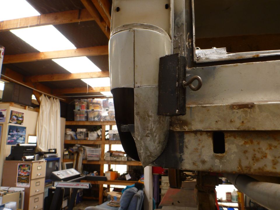 Close-up of rusty vehicle chassis with a metal bracket and loop attached.