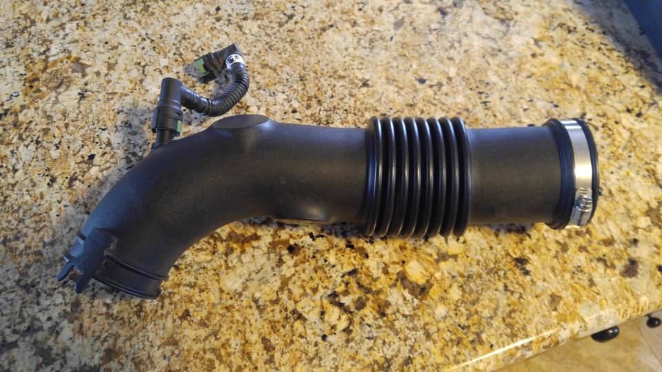 Black air intake hose with a ribbed section and a metal clamp