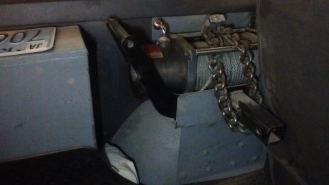 1985 Ford Bronco - A winch mechanism with a coiled cable and a heavy chain is mounted inside a vehicle.