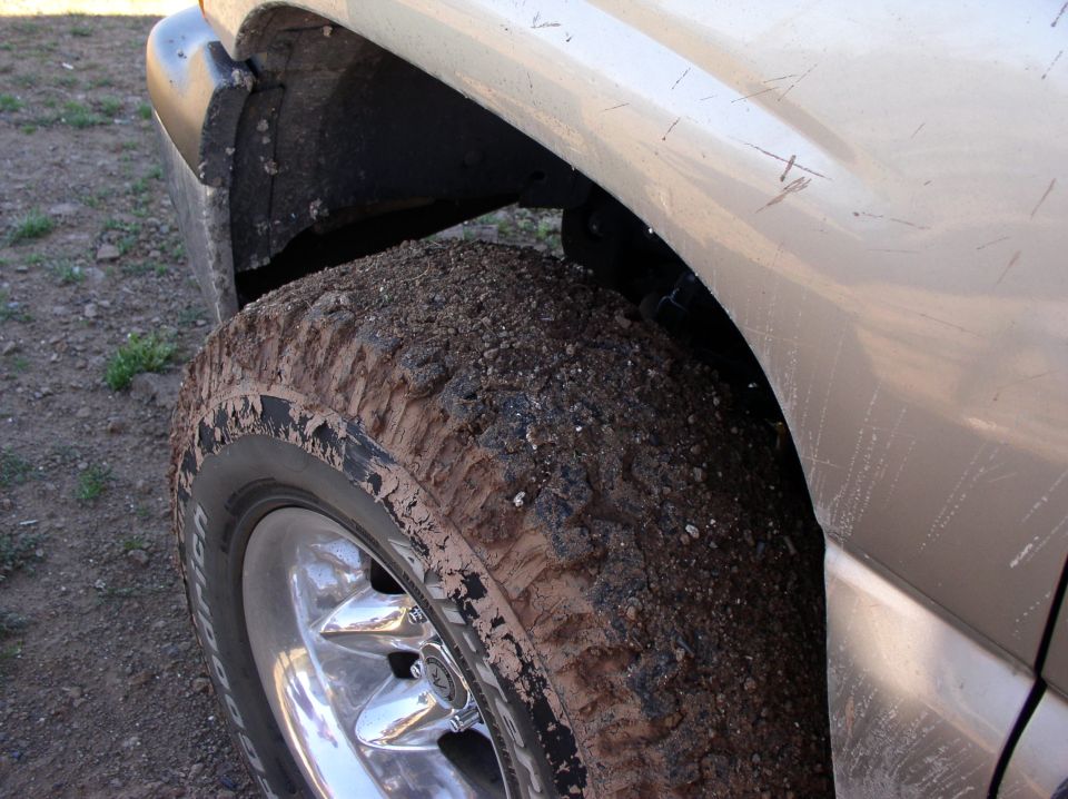 Mud-caked off-road tire and fender of a light-colored truck