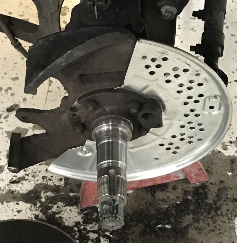 Close-up of a vehicle's front wheel hub assembly with a new brake rotor dust shield installed