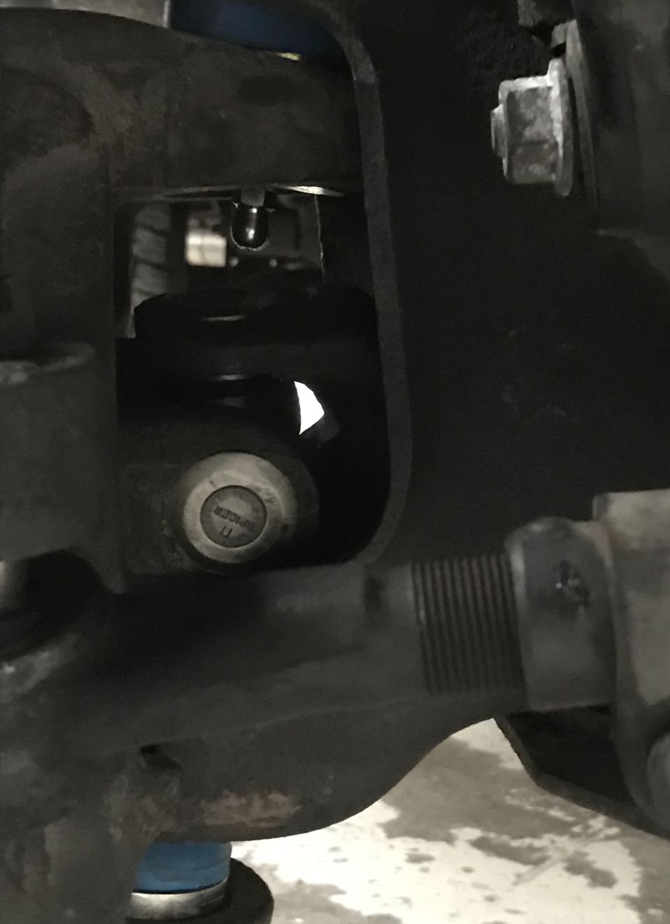 Close-up of a vehicle's suspension part with visible bolt head. Text on bolt reads 'DANGER 11'