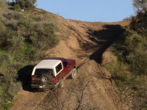 1990 Ford Bronco - A red and white Ford Bronco navigates an off-road dirt path on a sunny day.