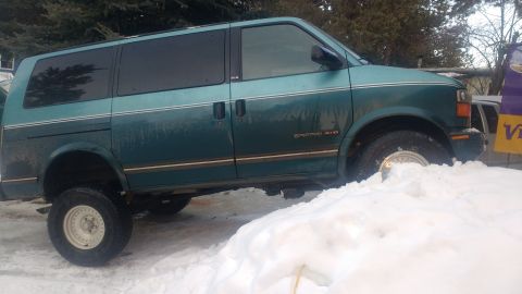 1995 GMC Safari - A lifted 1995 GMC Safari van is partially buried in snow, showing its side profile.