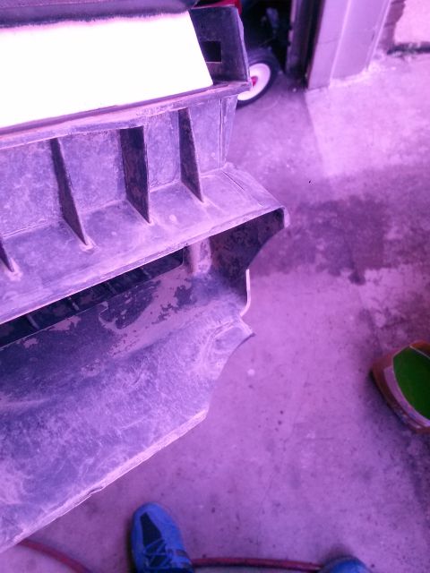 1996 Ford Bronco - Close-up of a dirty engine air intake component with a red hose in the foreground.