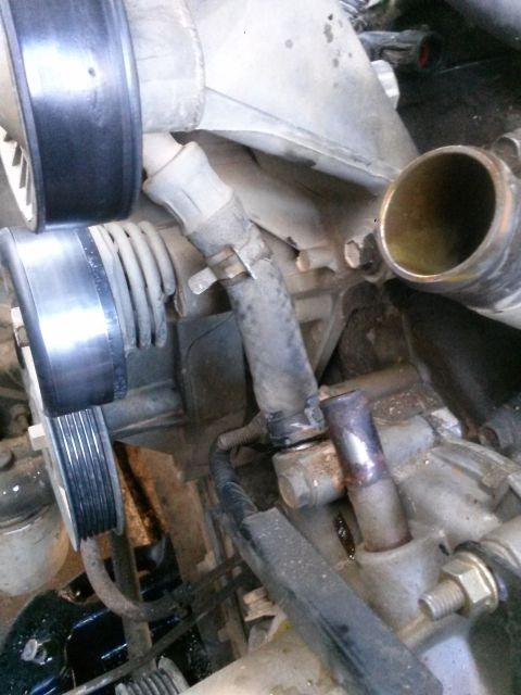 1996 Ford Bronco - Close-up view of engine components, including hoses, pulleys, and metal pipes, likely during a repair or maintenance procedure.