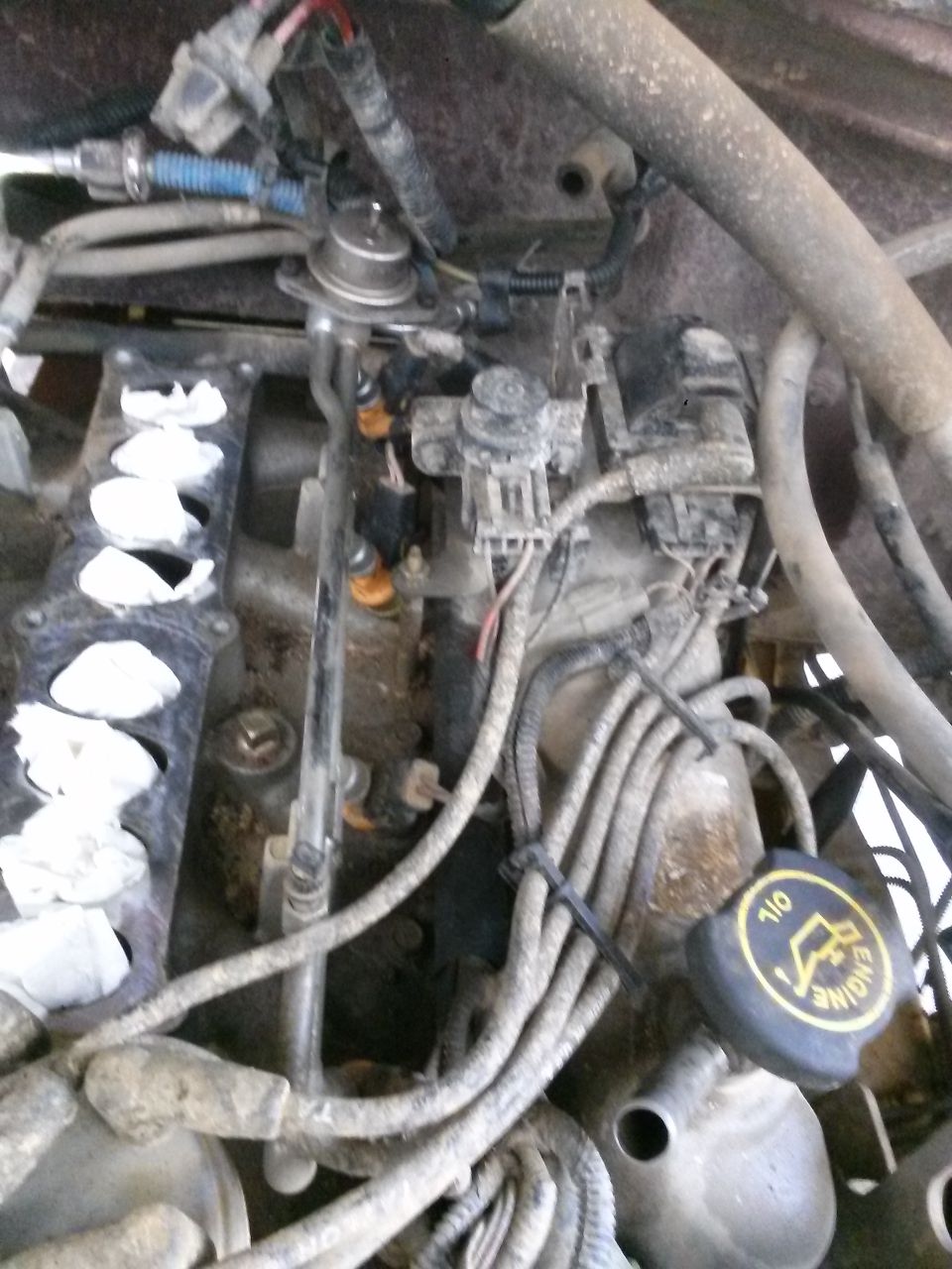 Engine bay with fuel rail, injectors, and wiring harness visible. Oil cap on right
