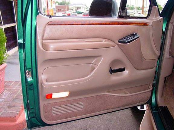 Tan Ford door panel with woodgrain trim and black power window switches on green truck
