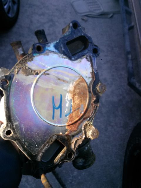 1996 Ford Bronco - A heavily corroded water pump is held for inspection, showing signs of wear and tear.