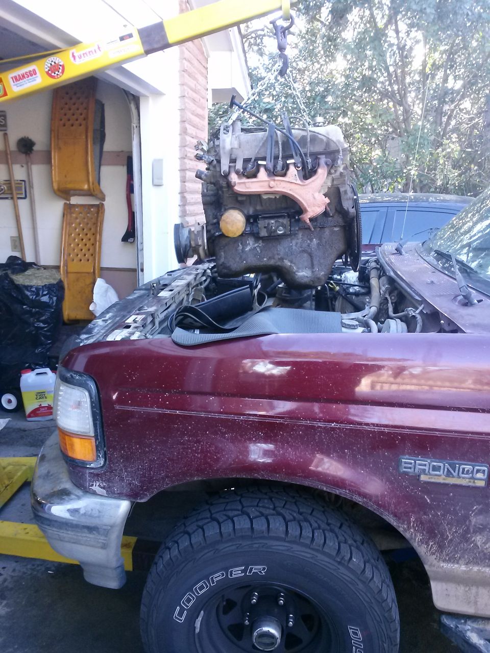 Engine being lifted out of a maroon Ford Bronco with a yellow engine hoist