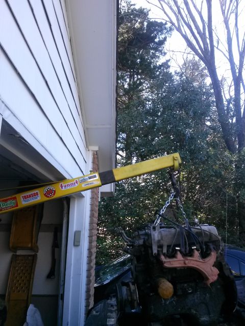 1996 Ford Bronco - An engine is being lifted by a yellow engine hoist outside a garage.