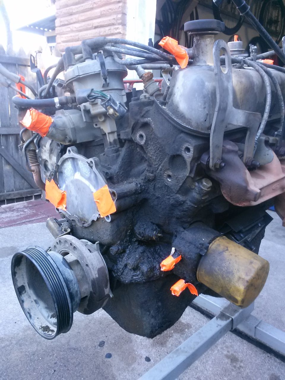 Engine block with distributor, hoses, and pulley. Orange tape covers some openings