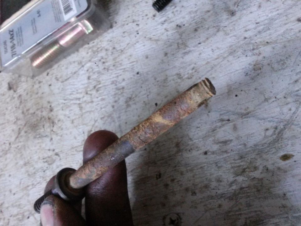 Rusted bolt held by a hand, with a package of bolts in the background