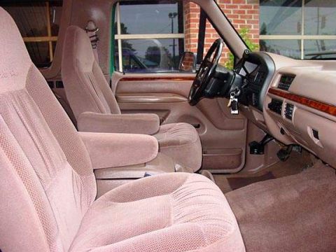 1996 Ford Bronco - The interior of a truck shows plush front seats and a wood-trimmed dashboard.