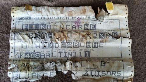 1996 Ford Bronco - A damaged vehicle identification document with various codes and alphanumeric strings printed on it.