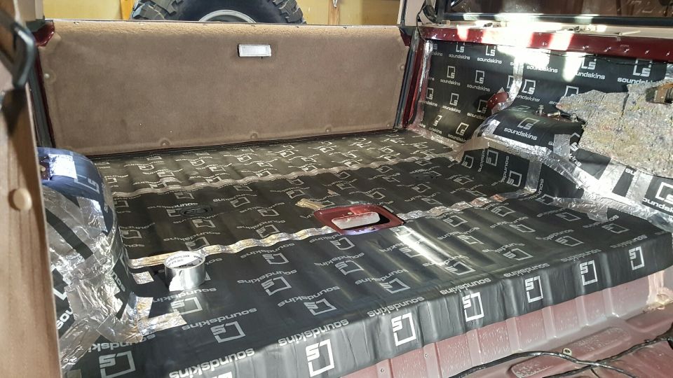Interior of a vehicle with sound deadening material applied to the floor and rear panels. A spare tire is visible above
