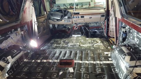 1996 Ford Bronco - The interior of a maroon SUV is being fitted with sound deadening material, revealing the dashboard and speakers.