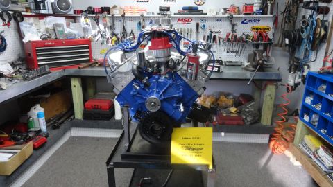 1982 Ford Bronco - A V8 engine is displayed on a stand in a workshop filled with tools and storage.