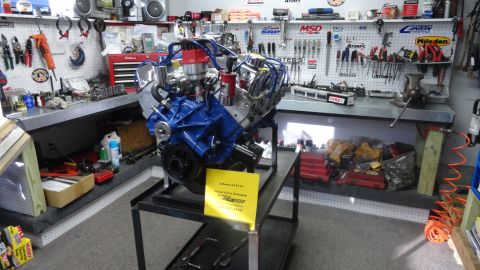 1982 Ford Bronco - A blue engine is displayed on a stand in a workshop, with tools and equipment visible in the background.