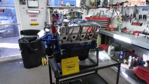 1982 Ford Bronco - V8 engine on display in a workshop setting with tools and equipment in the background.