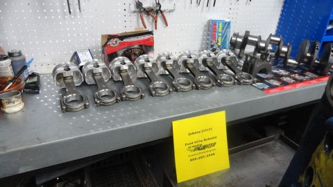 1982 Ford Bronco - Engine components, including pistons and connecting rods, are arranged on a workbench next to engine parts and tools.