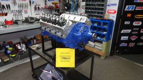 1982 Ford Bronco - A blue V8 engine is displayed on a stand in a cluttered workshop environment.