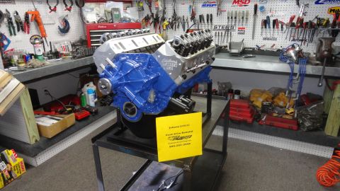1982 Ford Bronco - A V8 engine, identified by a yellow sign as a Ford 427, is displayed in a workshop setting.