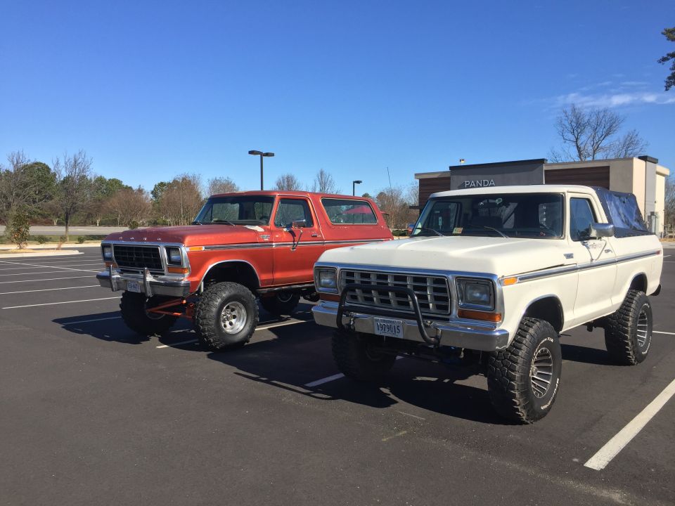 Orange and white Ford Broncos parked in a lot. The white one has a license plate that reads 199915