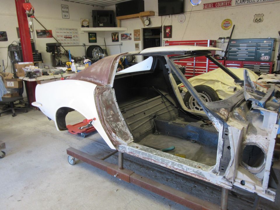 car body on a stand in a garage, undergoing restoration. White fender, rusty panels, interior stripped
