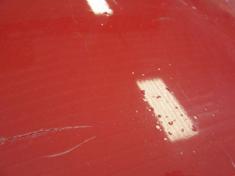 1976 Chevrolet Corvette - Close-up of a red car hood with visible scratches and water spots.