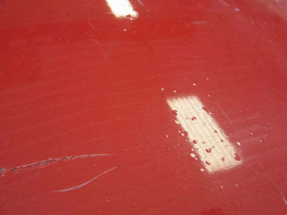 Red car hood showing scratches and reflections. SUPERMOTORS.NET logo visible