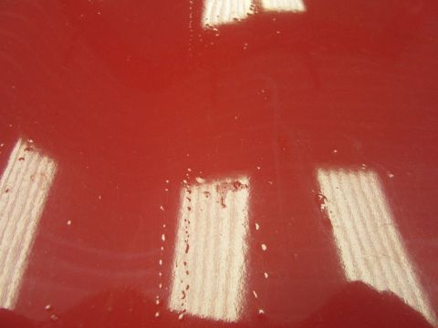 1976 Chevrolet Corvette - Reflections and water droplets are visible on the shiny red surface of a vehicle part.