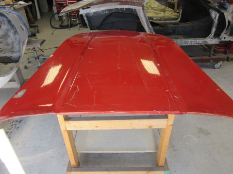 1976 Chevrolet Corvette - A red car hood is shown in a workshop, with other vehicle parts in the background.
