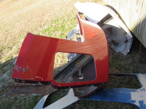 1976 Chevrolet Corvette - A red fender part, possibly from a Corvette, displays a wood grain texture beneath its chipped paint.