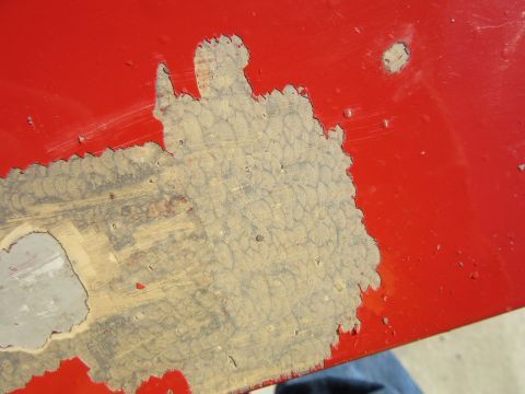 1976 Chevrolet Corvette - The red paint is peeling off, exposing the underlying material and texture of the car panel.