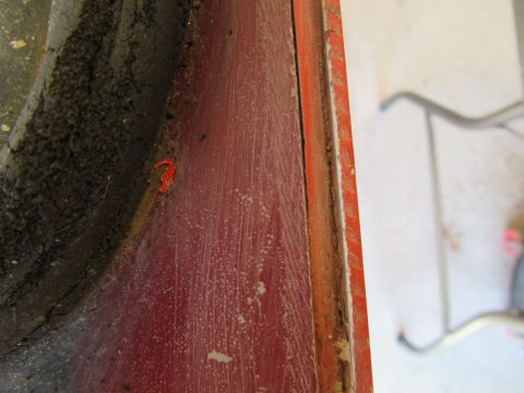 1976 Chevrolet Corvette - A close-up view of a section of red painted metal, revealing dirt, dust, and a small orange fragment.