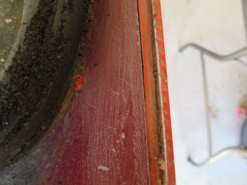 Close-up of red painted metal with dirt and a small orange piece, showing a seam and some dust