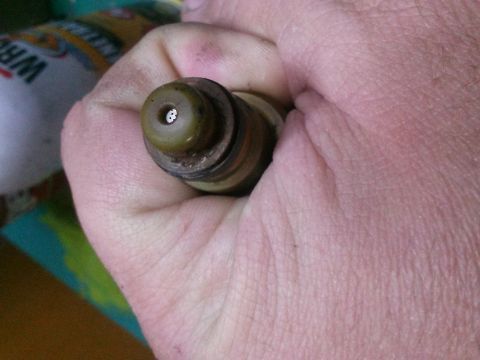 1996 Ford Bronco - A close-up view of a fuel injector being held in a hand, showing its nozzle and some wear.