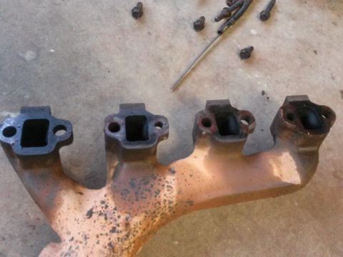 1996 Ford Bronco - An exhaust manifold is shown with its ports open, lying on a concrete surface with loose bolts.