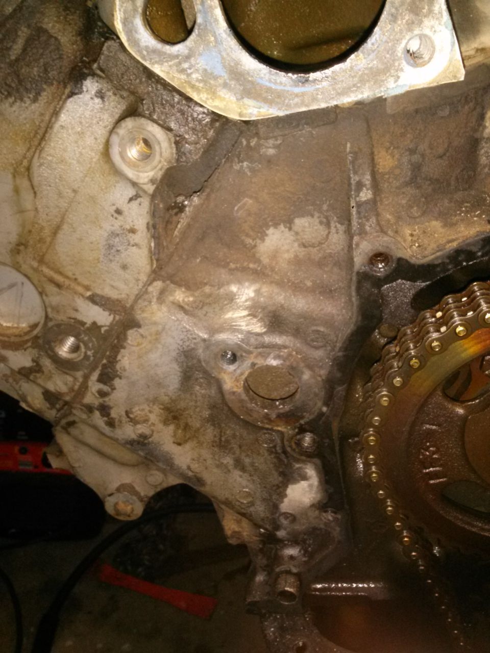 Engine block with timing chain and gears, showing oil residue and bolt holes