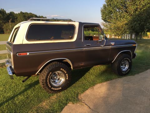 1978 Ford Bronco - A brown and white 1978 Ford Bronco is shown from the side, parked on a grassy area with trees in the background.